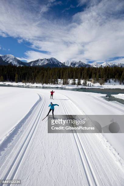 een vrouw leidt een man op een cross-country skate-ski in de rocky mountains van british columbia, canada. - heteroseksueel koppel stockfoto's en -beelden