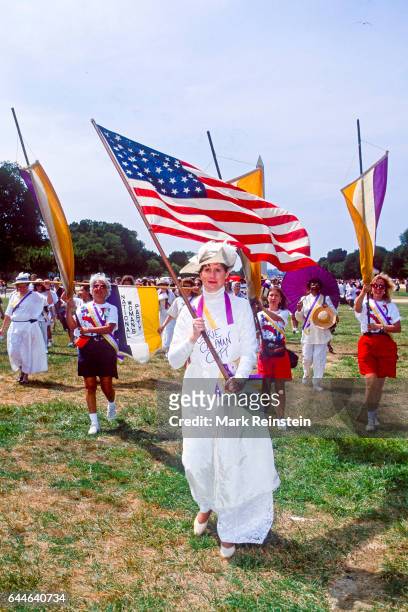 View of marchers, among them one dressed as Carrie Chapman Catt who carries an American flag, during a rally in honor of the 75th anniversary of the...