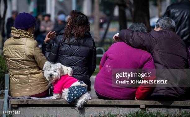 People sit on a bench in the sun in Shanghai on February 24, 2017.