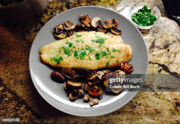 sole meuniere in a plate with sauteed portabella mushrooms, garnished with mincedflat leaf parsley from a small bowl - sogliola foto e immagini stock