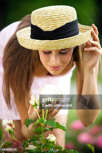 Junge Frau mit Strohhut bewundert eine Rose, young woman hatted admiring a rose