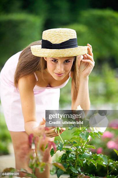 Junge Frau mit Strohhut bewundert eine Rose, young woman hatted admiring a rose