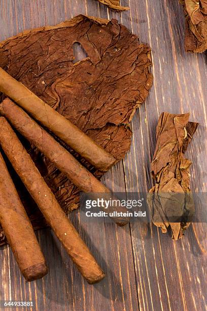 Blätter von Tabak und fertige Zigarren liegen nebeneinander.