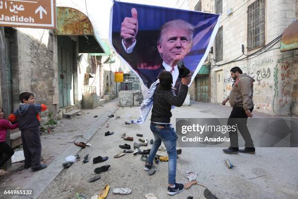 Palestinians hit a US President Donald Trump poster to condemn Trump's policies as they stage a protest against Israeli Government's violations over...