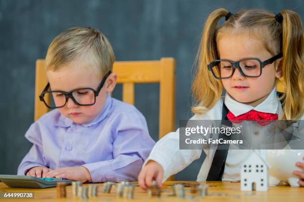 zwei kleinkinder sind als geschäft erwachsene verkleidet. sie sind zählen geld und münzen in ein sparschwein. - blonde girl piggy bank stock-fotos und bilder