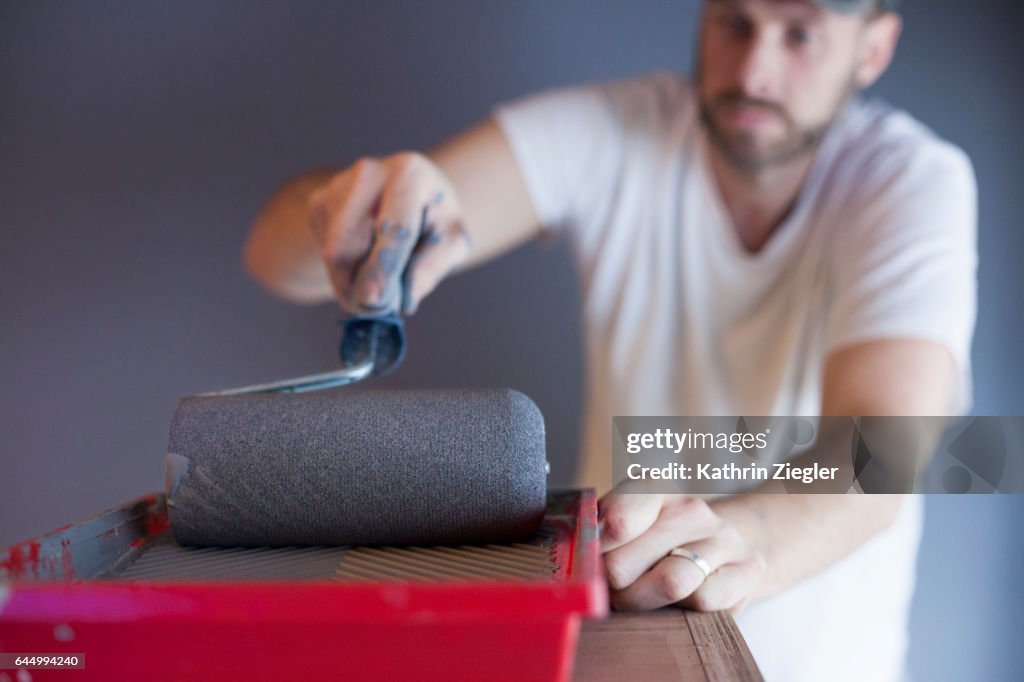 Man using paint roller to paint the walls with gray color