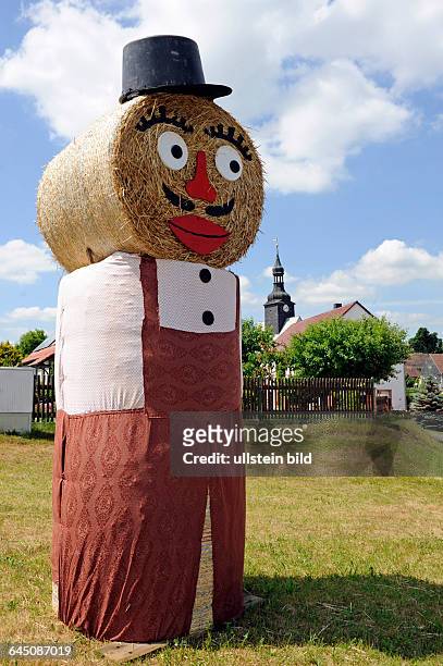 Aus Strohrollen lustig gefertigter Strohmann am Dorfeingang symbolisiert das Erntefest der laendlichen Bevoelkerung des Ortes