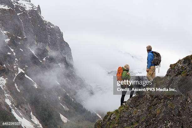 hiking couple look off to misty peaks from ridge - grindelwald stock pictures, royalty-free photos & images