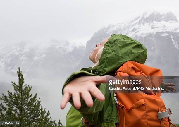 female hiker spreads arms to embrace mountain mist - grüne jacke stock-fotos und bilder