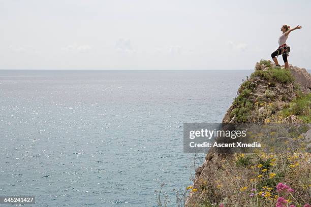 female rock climber spreads arms above climb, sea - woman cliff stock pictures, royalty-free photos & images