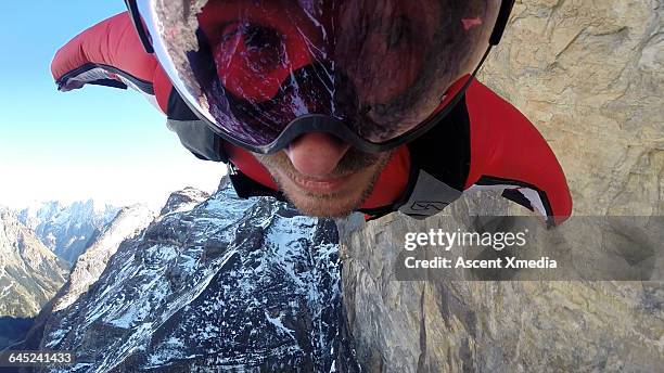 wingsuit flier airborne over mountain face - aviation risk stock-fotos und bilder