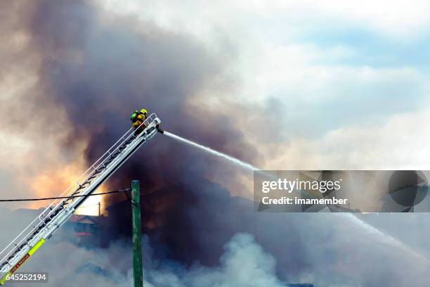 firefighter spraying water on burning house, background with copy space - firefighter stock pictures, royalty-free photos & images