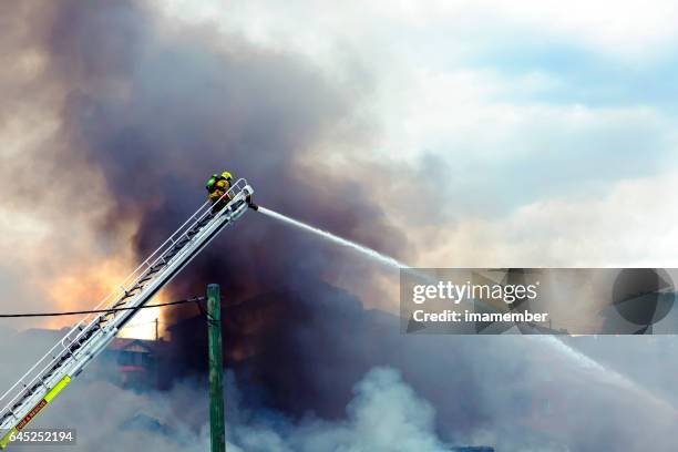 firefighter spraying water on burning house, background with copy space - emergency services australia imagens e fotografias de stock