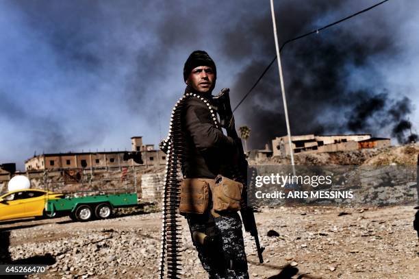 Smoke rises in the background as members of Iraq's elite Rapid Response Division hold position in the northern city of Mosul as they continue the...