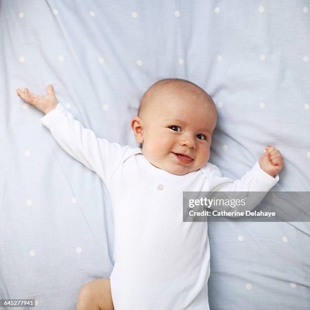 a 4 month old baby boy laying on a bed - strampelanzug stock-fotos und bilder