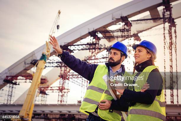 teamwork in construction industry - two engineers working together on construction site with blueprints and plans - serbia bridge stock pictures, royalty-free photos & images