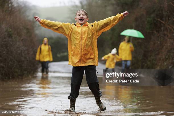family in rain, boy jumping in puddle - frau mit gelben regenmantel stock-fotos und bilder