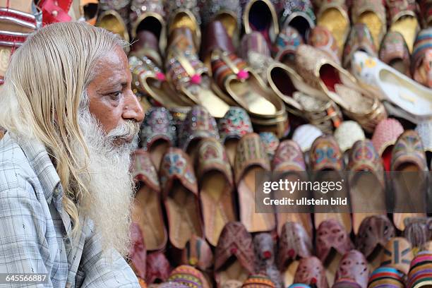 Ein Straßenhändler vor seiner Auswahl an traditionellen indischen Schuhen auf dem Markt in Sarojini Nagar in Neu Delhi