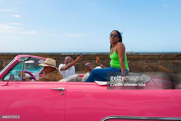 Zwei Männer fotografieren in einem Oldtimer Cabrio der 1950er Jahre aus den USA am in der Altstadt von Havanna, Kuba, eine Frau auf dem Rücksitz des...