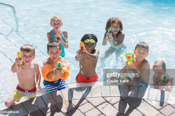 multi-ethnic group of children in pool with squirt guns - kids pool games stock pictures, royalty-free photos & images