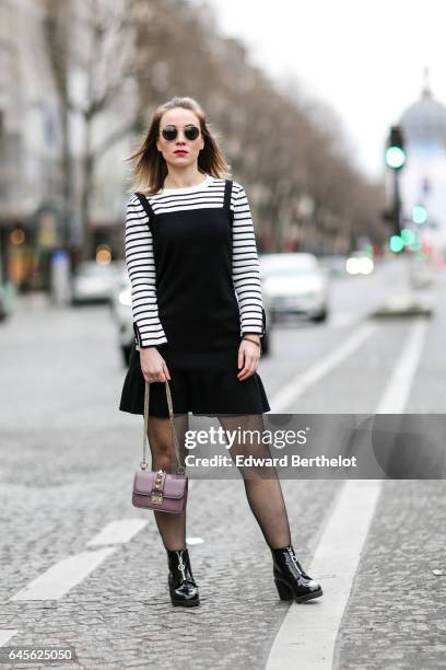 Amelie Lloyd, fashion blogger, wears sunglasses, a Dahlia Girls black dress with a striped collar, fishnet tights, a Valentino rockstud bag, and New...