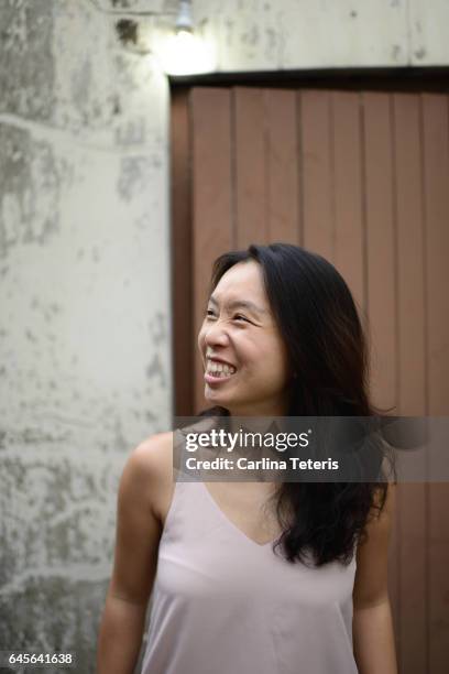young woman smiling in an alley way under a light bulb - singapore alley stock pictures, royalty-free photos & images