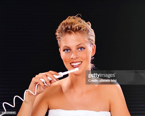 Blonde Frau putzt sich die Zaehne mit einer elektrischen Zahnbürste,