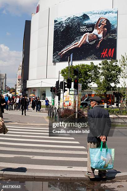 In der Bukarester Innenstadt steht ein Mann an einer Ampel und wartet auf grün. Im Hintergrund hängt ein Riesenplakat mit H&M Werbung.