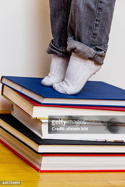 Kind steht auf einem Stapel Bücher, Symbol für Schulbildung, Lesekompetenz, Lernförderung