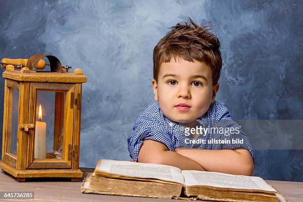 Kleiner Junge mit altem Buch und Windlicht, Symbol für Bildung, Schulreform, Lernen
