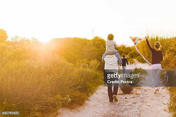 rear view of family walking on sandy footpath - beach walking stock-fotos und bilder