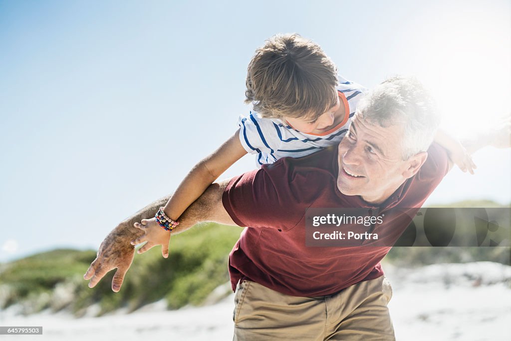 Excited father giving piggyback to son at beach