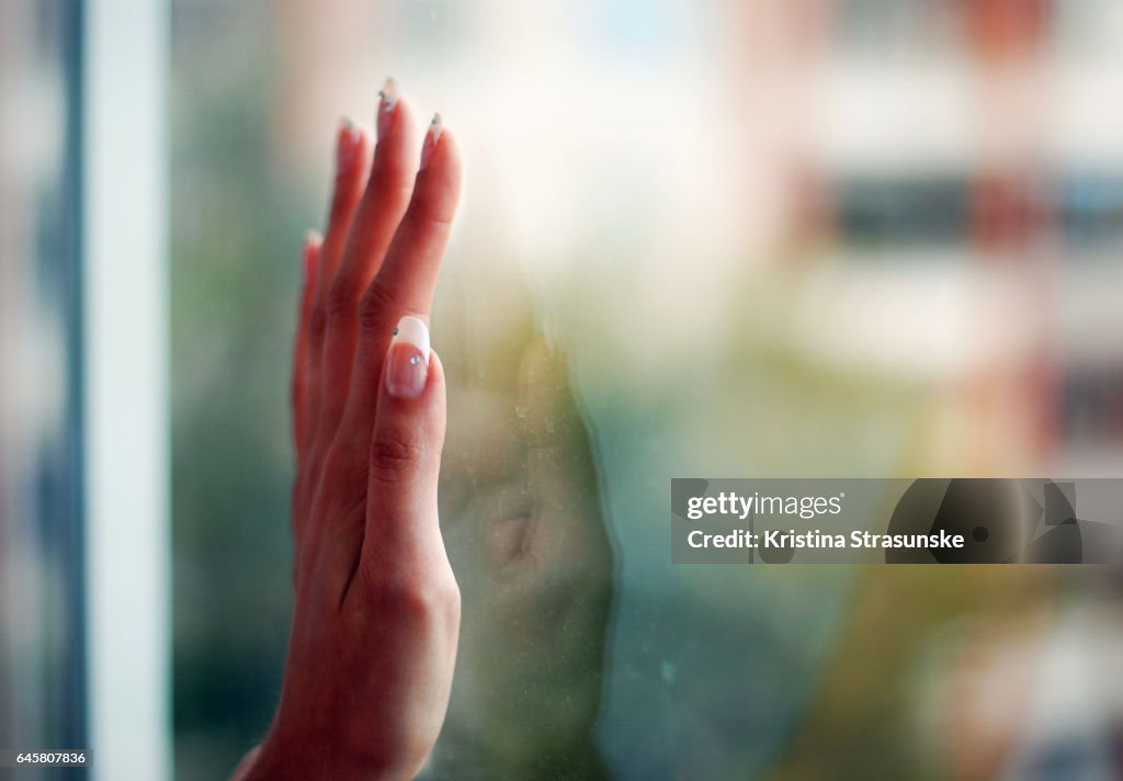 Woman's hand with manicured nails reflected in a window