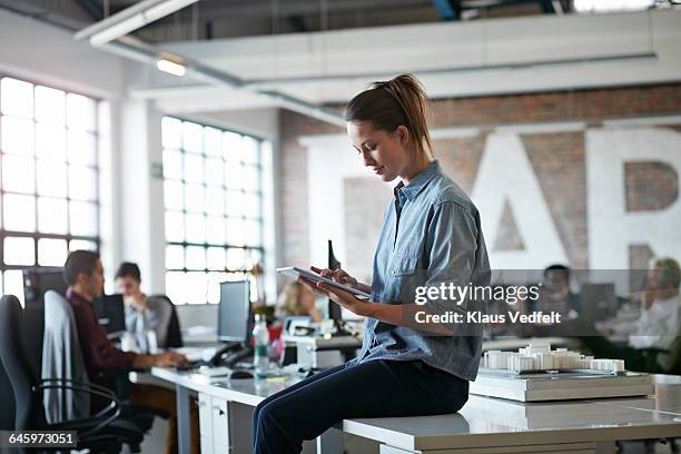 woman sitting on desk with tablet at, open office - creative desk ストックフォトと画像