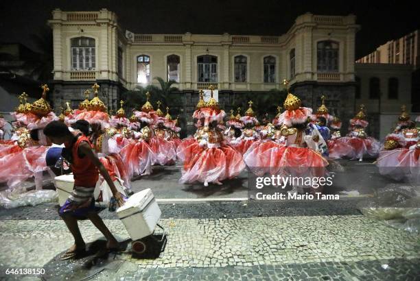 Revelers from the Portela samba school wait to perform as a street vendor walks past outside the Sambodrome in the early morning hours during...