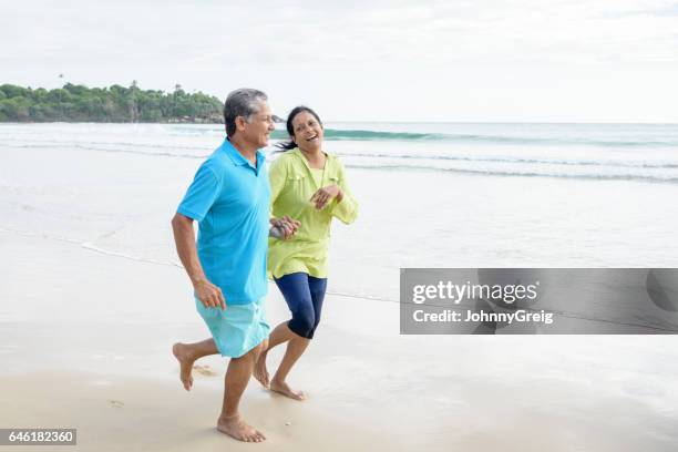 senior man and mature woman laughing and jogging on beach - cultura cingalesa imagens e fotografias de stock