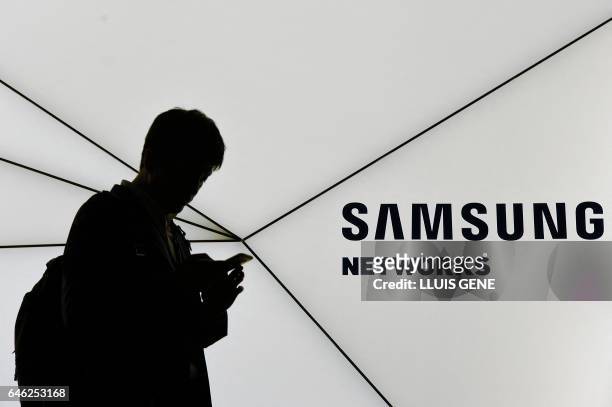 Visitor uses his mobile phone as he walks past the stand of Samsung on the second day of the Mobile World Congress in Barcelonaon on February 28,...