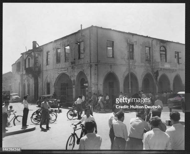 Aftermath In Nicosia. Sightseers gather round to look at the damage to the gutted building of the British Institute in Nicosia which was set on fire...
