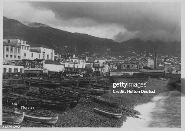 Quayside view of rowboats on a pebble beach, on the coast of a Madeiran island.