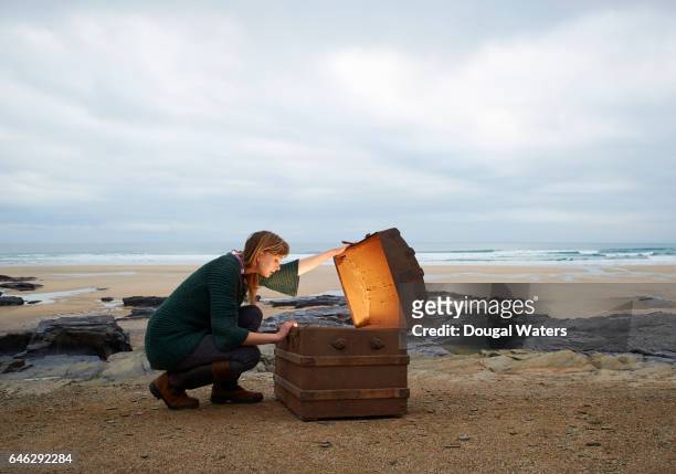 woman looking inside treasure chest on deserted beach. - scoperta foto e immagini stock