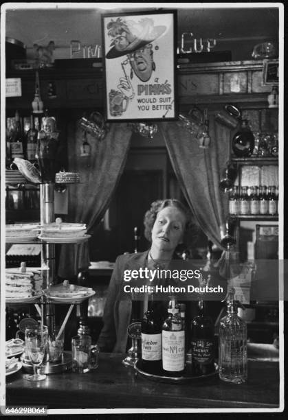 Winkie Hunt, the wife of the licensee of The Hour Glass pub, at work behind the bar. | Location: The Hour Glass, Brompton Road, Kensington, London,...