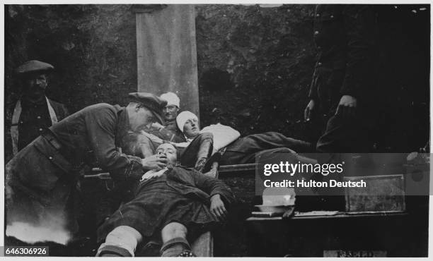 Medic gives a wounded soldier a drink of water, other injured soldiers, their heads in bandages, look on. The medical facilities in the trenches were...