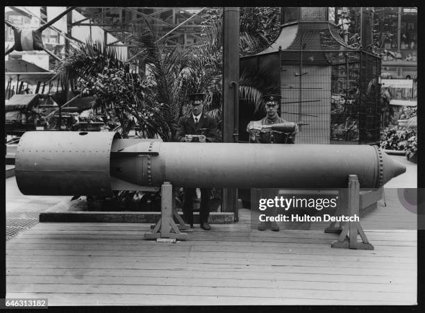 Military officers at the Imperial War Museum in London stand near the largest aerial bomb holding two of the smallest aerial bombs.