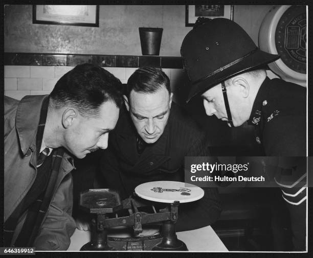 At the Metropolitan Police Training School at Peel House, a Sergeant instructs pupils on how to test suspected counterfeit coins by weighing them...
