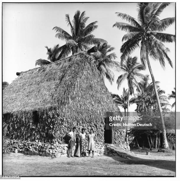 Islanders stand outside a large, thatched, hut.