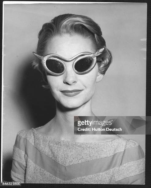 Model wears gilt plastic sunglasses, with snake rims. September 1956.