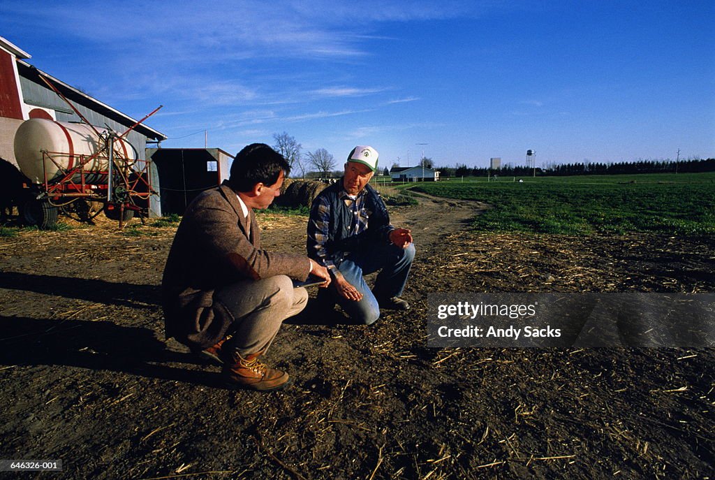 Businessman and farmer consulting at field edge,background buildings