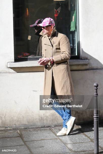Guest wears a pink cap, sunglasses, a beige coat, blue denim jeans pants, and white sneakers shoes, outside the JOUR/NE show, during Paris Fashion...