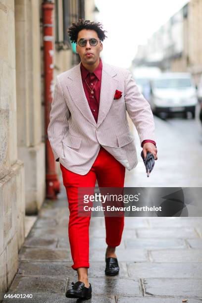 Guest wears sunglasses, a red shirt, a pink striped blazer jacket, red pants, and black leather shoes, outside the JOUR/NE show, during Paris Fashion...