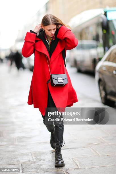 Guest wears a black Furla bag, a red coat, black pants and black boots, outside the JOUR/NE show, during Paris Fashion Week Womenswear Fall/Winter...